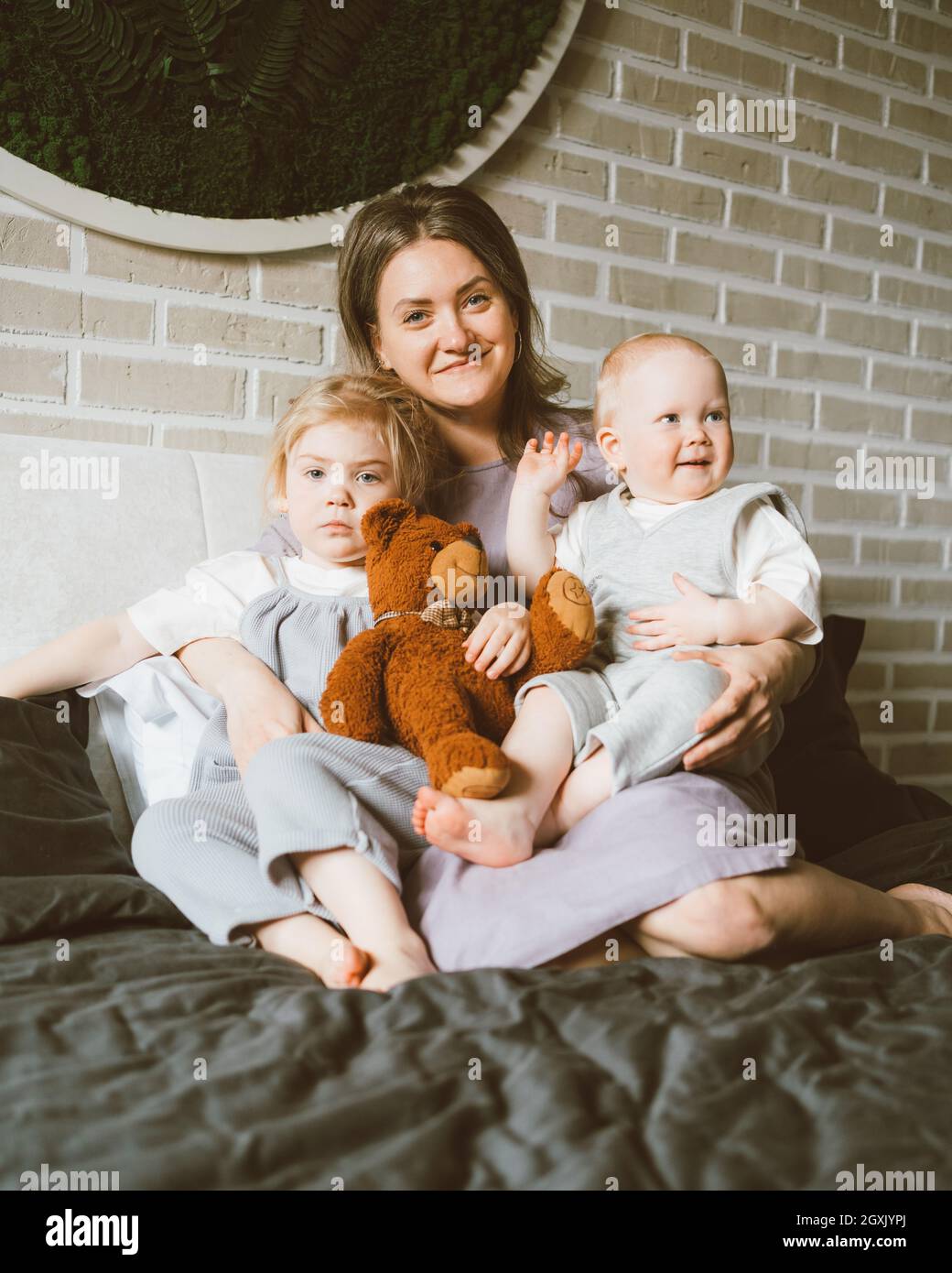 Felice madre con due bambini che si rilassano sul letto grande di casa Foto Stock