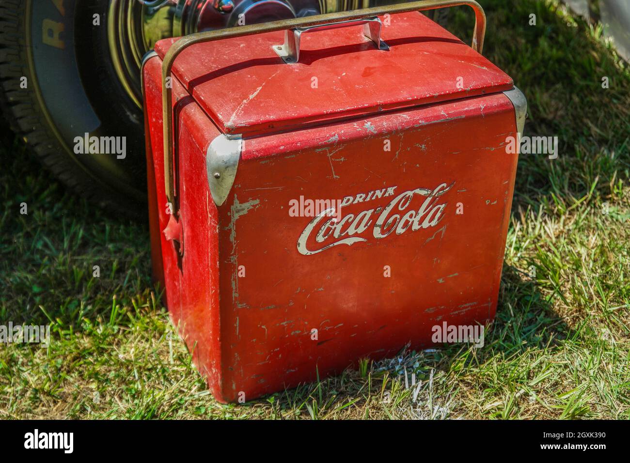 Un metallo retrò antico Coca-Cola di viaggio fresco con patina seduta a terra accanto a un'auto all'aperto sul primo piano di visualizzazione angolo Foto Stock