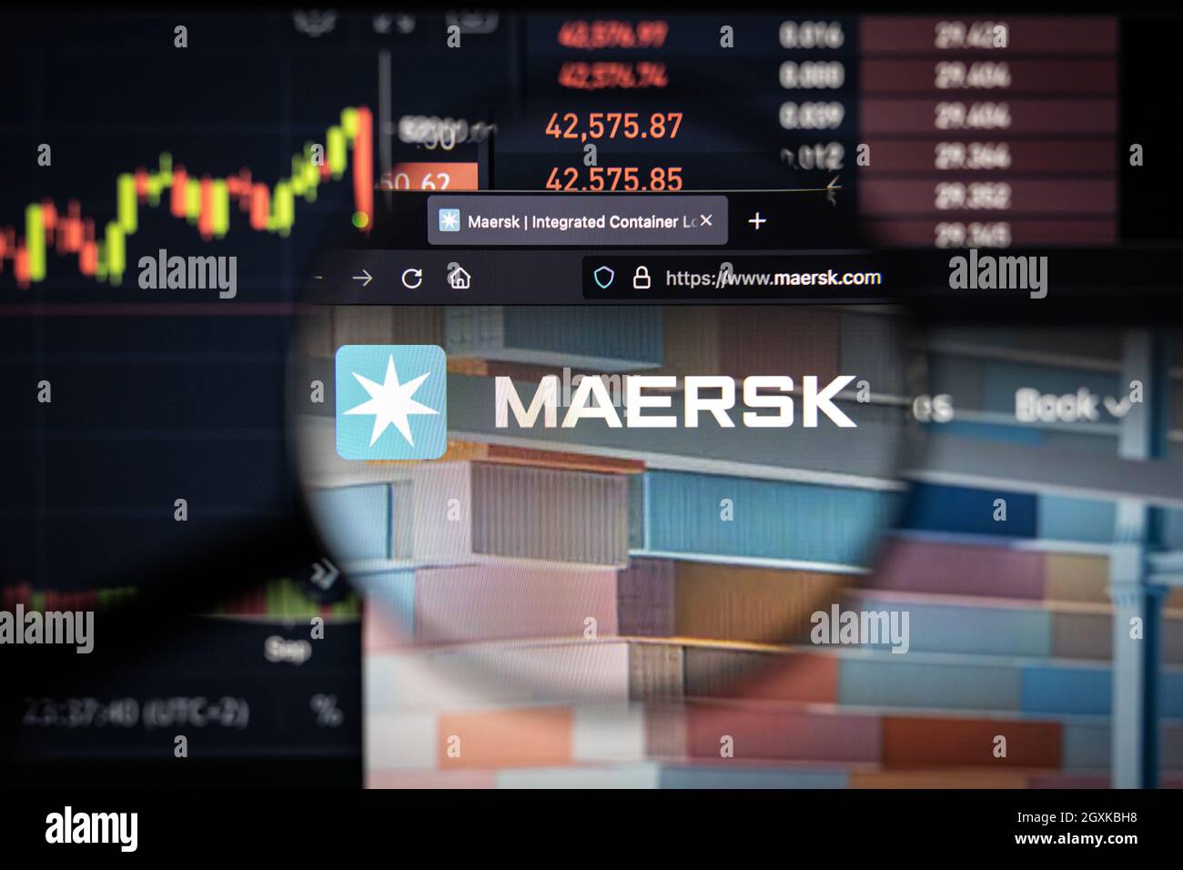 Maersk azienda logo su un sito web con blurry mercato azionario sviluppi in background, visto su uno schermo di computer attraverso una lente d'ingrandimento Foto Stock