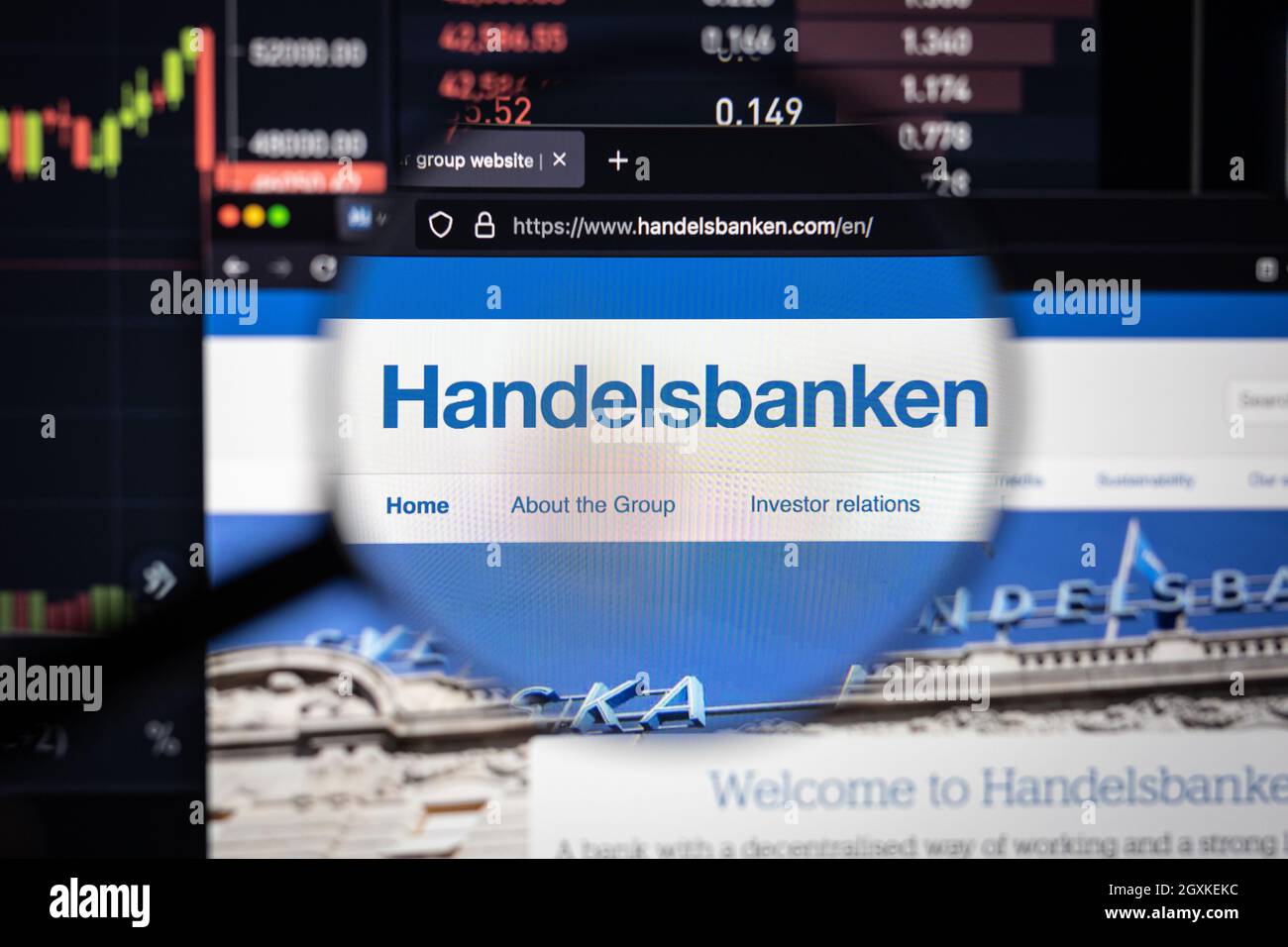 Handelsbanken azienda logo su un sito web con blurry sviluppi del mercato azionario in background, visto su uno schermo del computer attraverso una lente d'ingrandimento Foto Stock