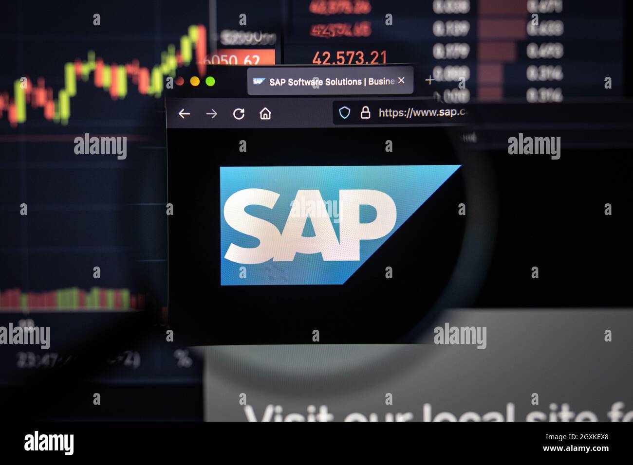 Logo aziendale SAP su un sito Web con sviluppi sfocati del mercato azionario sullo sfondo, visto su uno schermo del computer attraverso una lente di ingrandimento Foto Stock