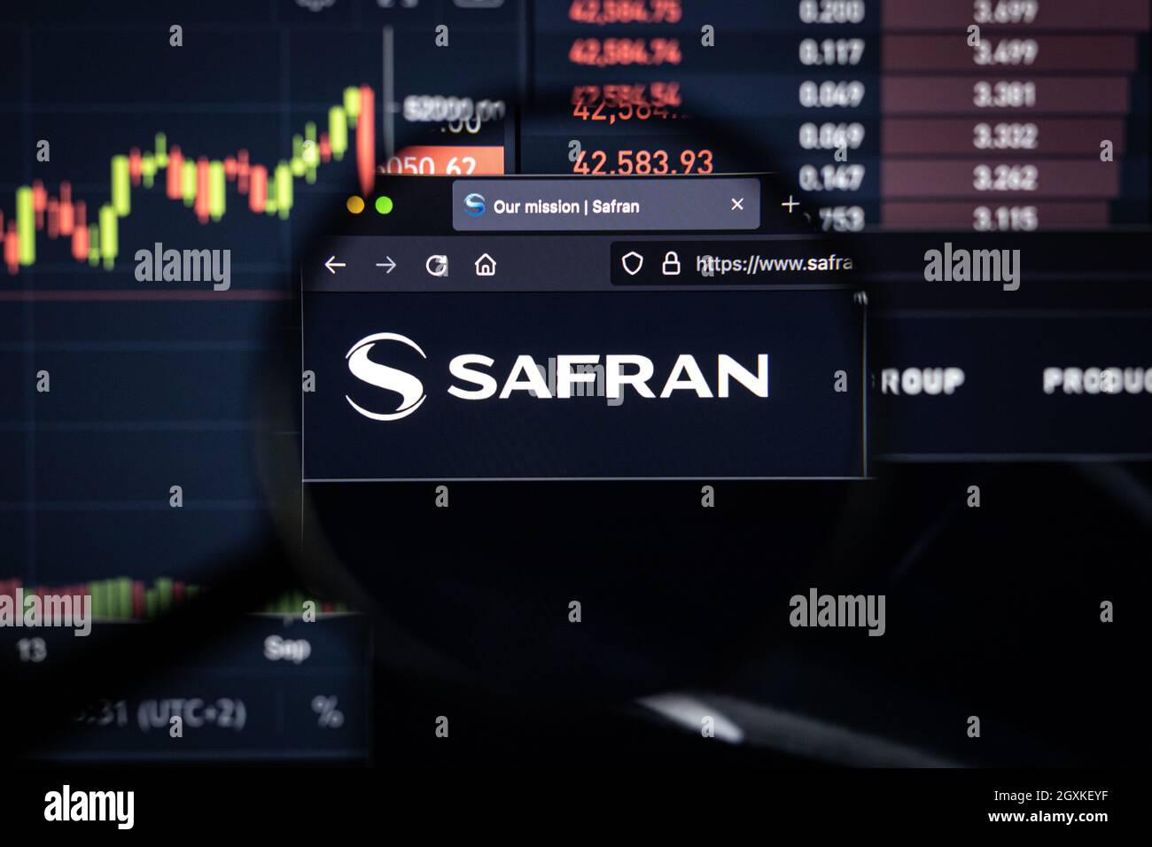 Safran Company logo su un sito web con blurry mercato azionario sviluppi in background, visto su uno schermo di computer attraverso una lente d'ingrandimento Foto Stock