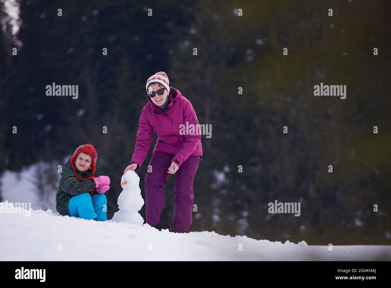 Felice famiglia giovane giocare nella neve fresca e costruzione di pupazzo di neve in bella e soleggiata giornata invernale outdoor in natura Foto Stock