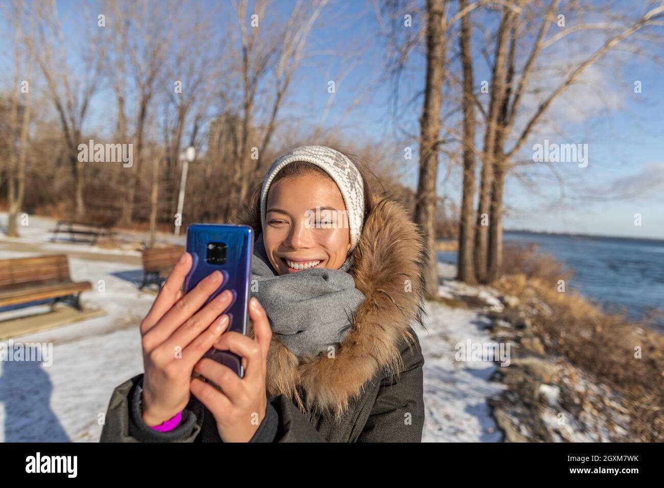 Inverno viaggio Asian turista donna prendendo selfie foto con telefono cellulare sulla natura foresta sentiero camminare tenere smartphone con mani senza guanti Foto Stock