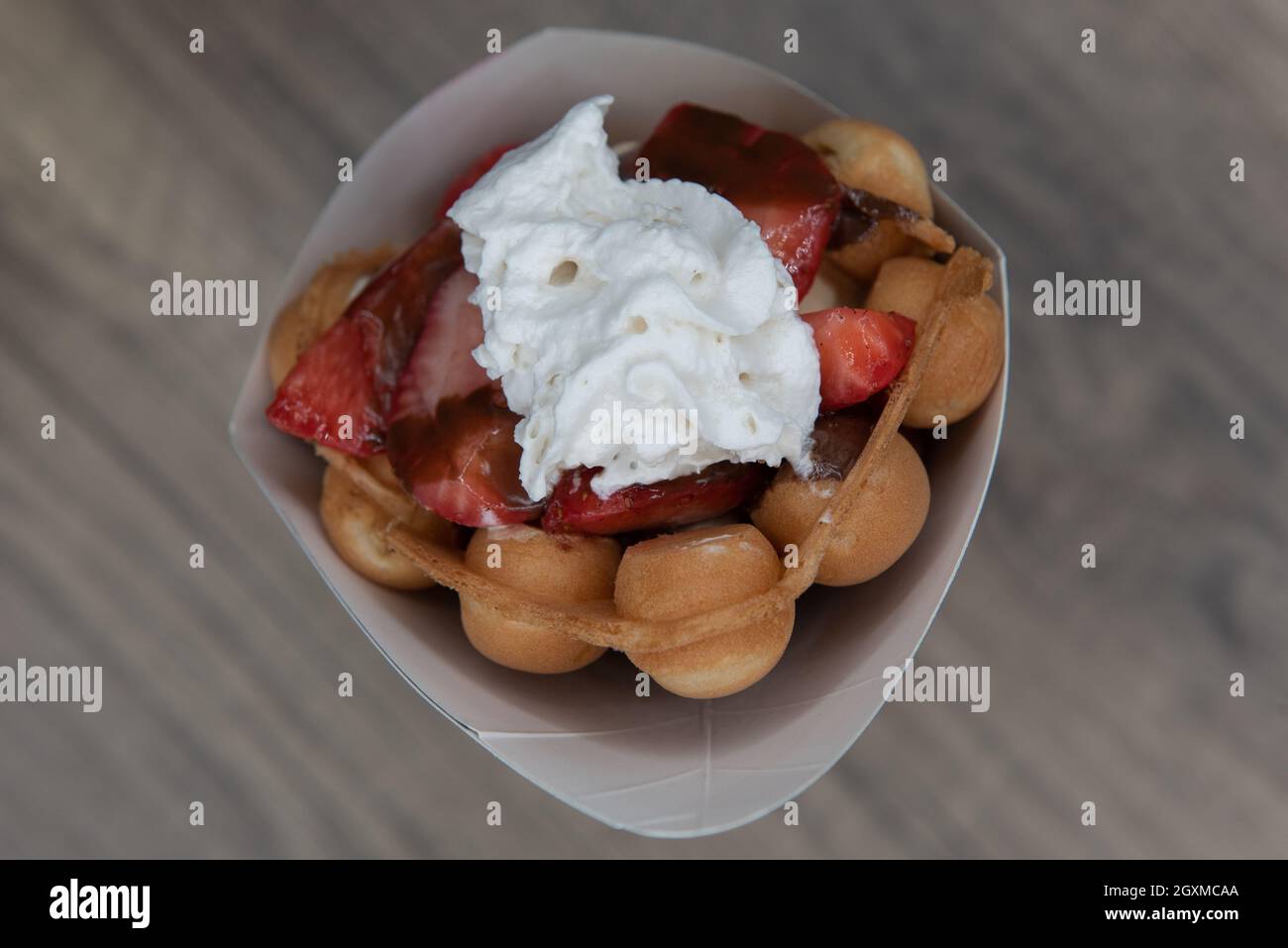 Vista dall'alto della frutta a cono con waffle con fragole affettate e guarnita con panna montata per un dessert perfettamente dolce. Foto Stock