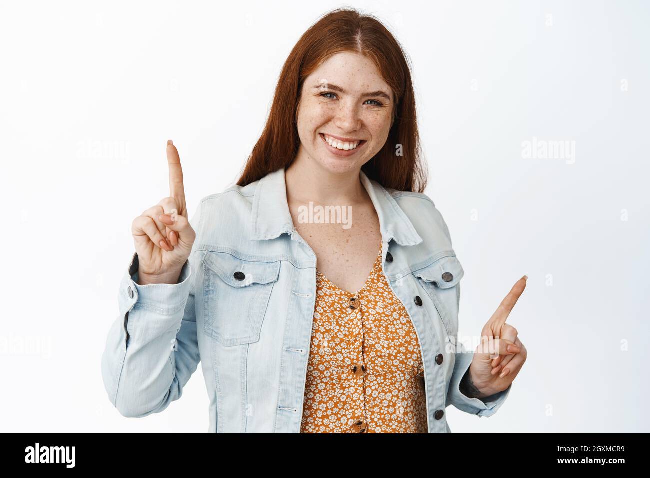 Donna sorridente felice con capelli rossi, puntando lateralmente, mostrando due scelte, varianti di opzioni, in piedi su sfondo bianco Foto Stock