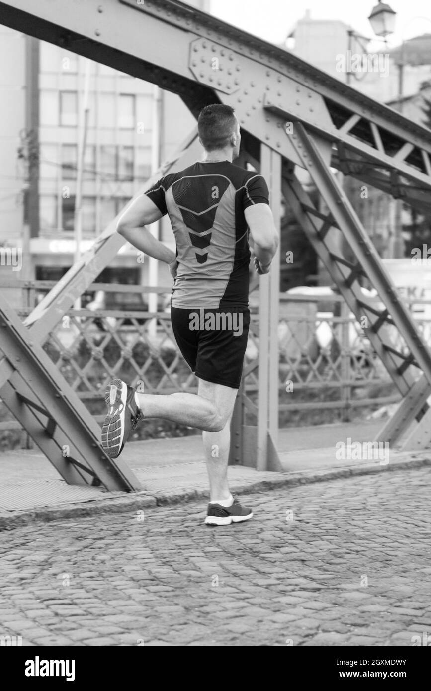 Urban sport, giovane uomo sano jogging attraverso il ponte in città al mattino presto nella notte Foto Stock