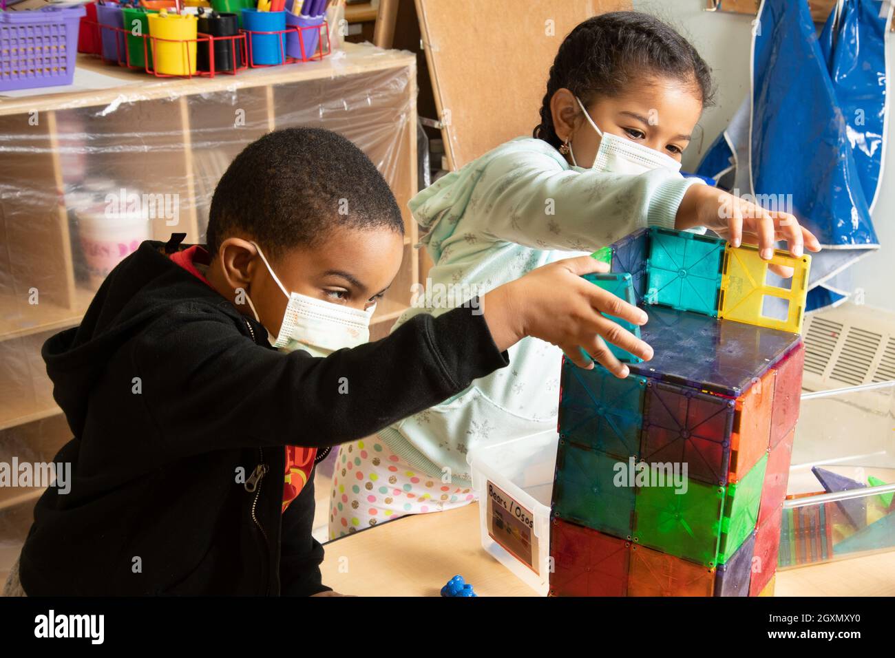 Istruzione Preschool 4-5 anni ragazzo e ragazza costruzione insieme con piastrelle magnetiche, indossare maschere per proteggere contro il virus Covid-19 Foto Stock