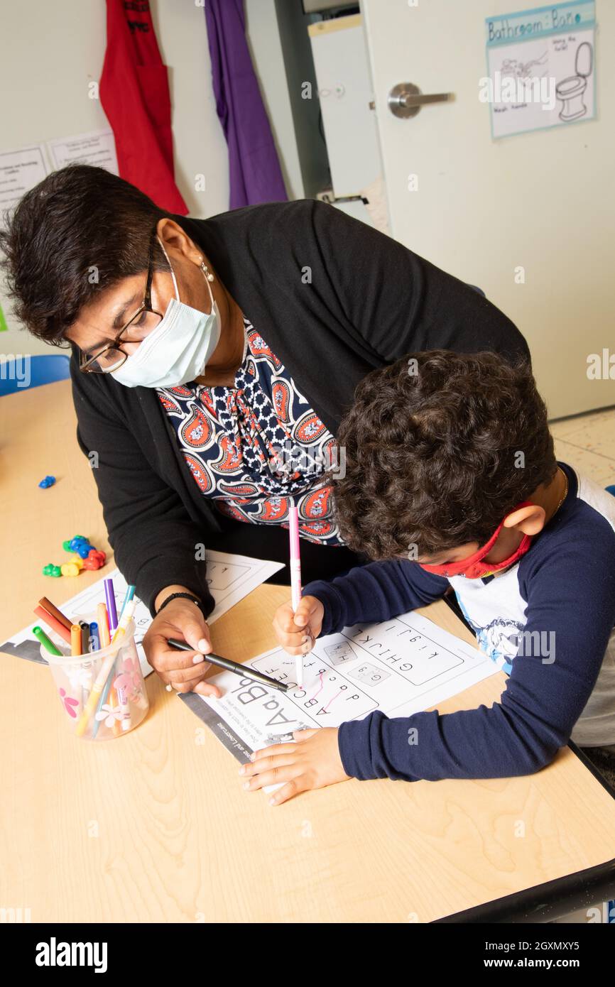 Istruzione Preschool 4-5 anni insegnante femminile lavora con il ragazzo utilizzando il marcatore per tracciare le lettere sulla scheda ABC indossando maschere per il viso per proteggere contro Covid-19 Foto Stock