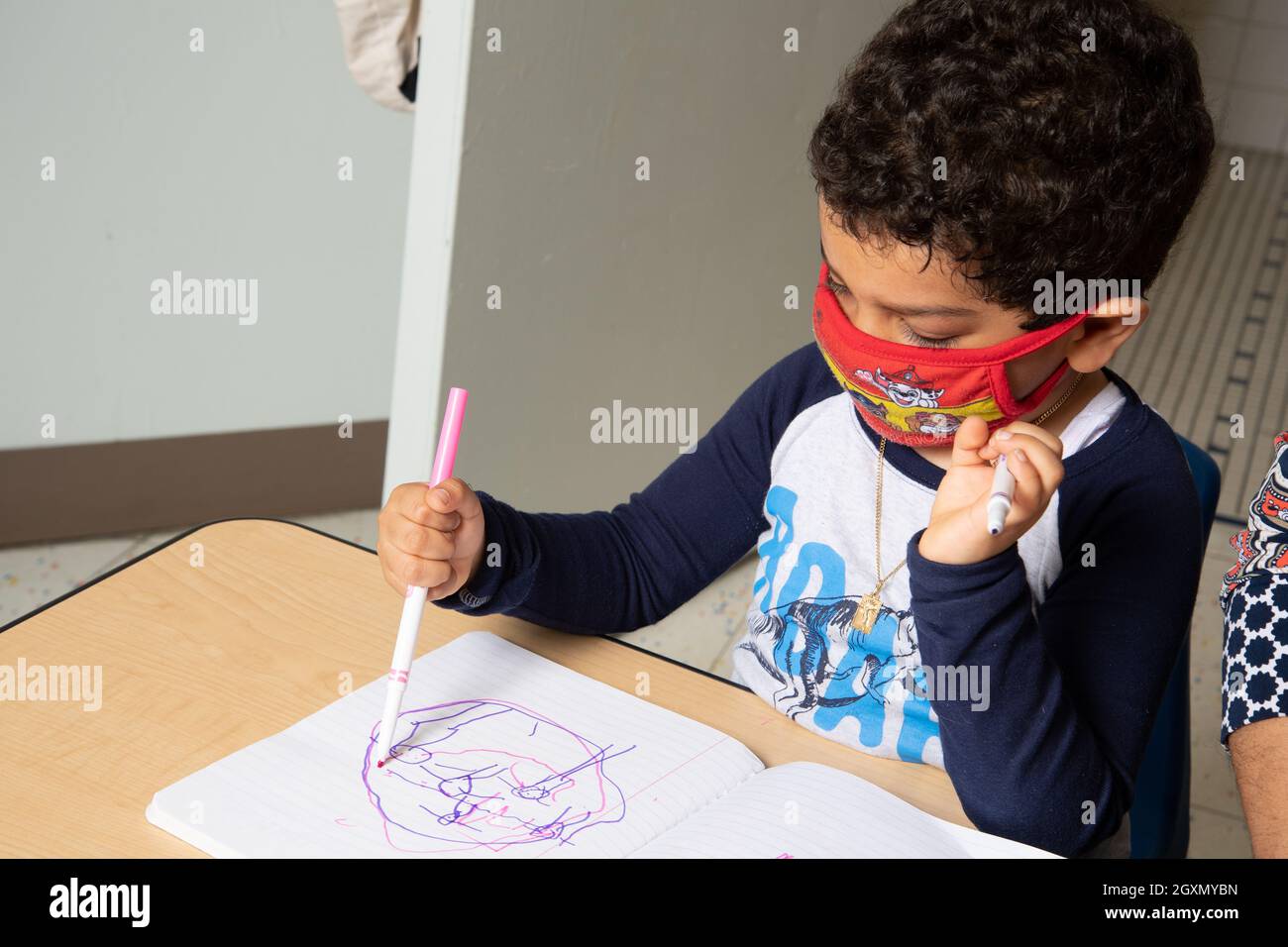 Istruzione Preschool 4-5 anni ragazzo seduto e disegno con marcatore tenuto in pugno impugnatura, indossare maschera per il viso per proteggere contro l'infezione Covid-19 Foto Stock