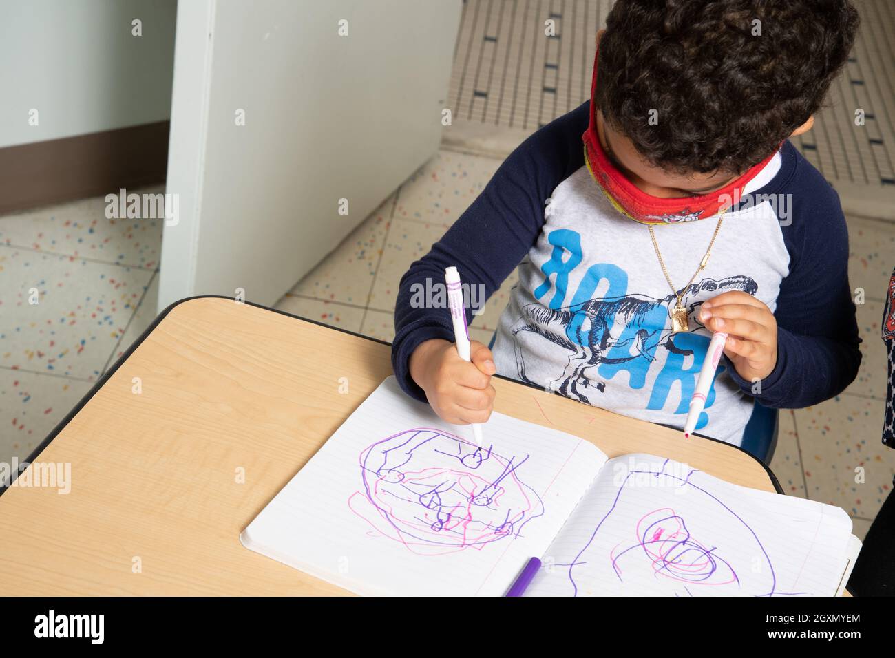 Istruzione Preschool 4-5 anni ragazzo seduto e disegno con marcatore tenuto in pugno impugnatura, indossare maschera per il viso per proteggere contro l'infezione Covid-19 Foto Stock