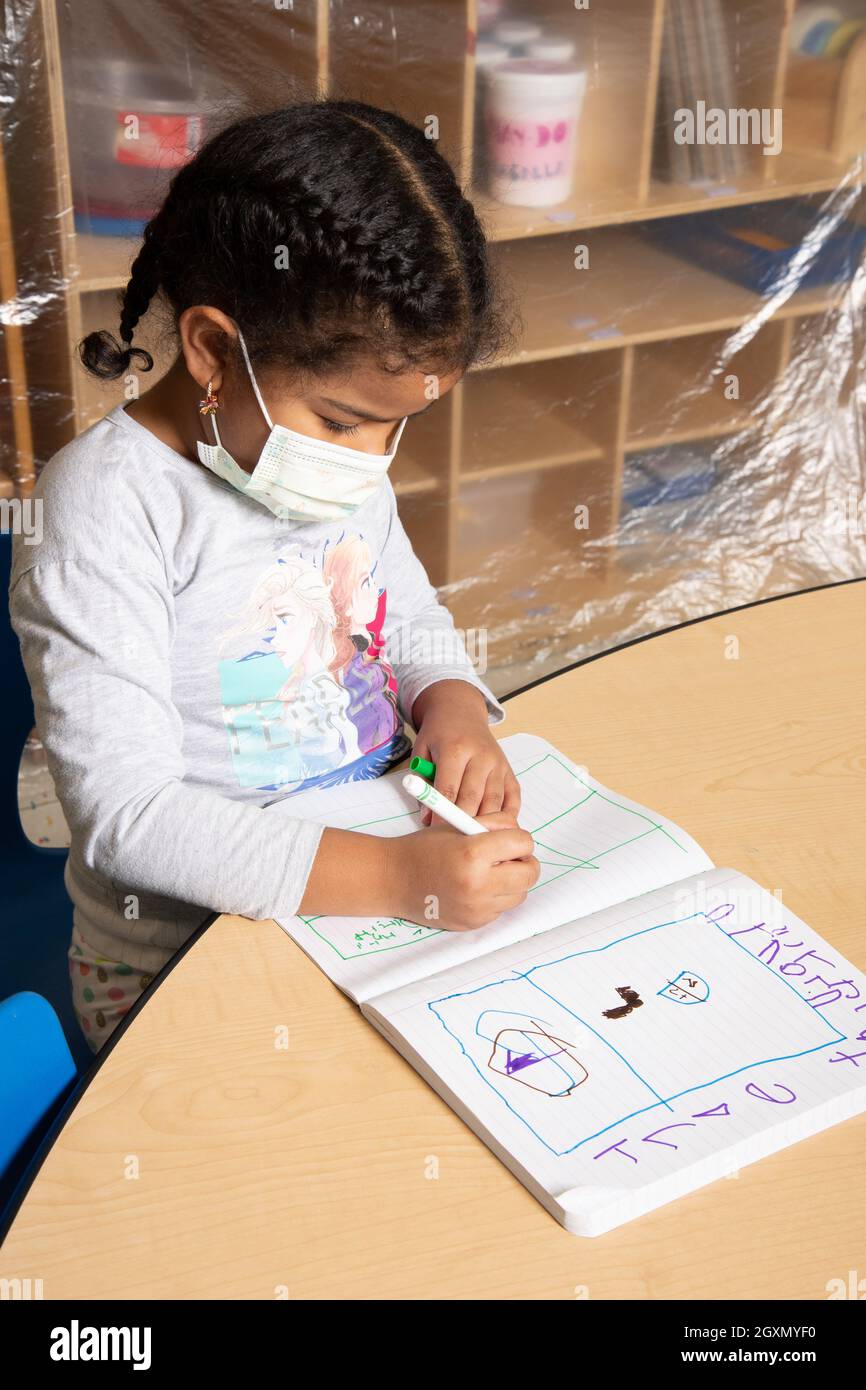 Istruzione Preschool 4-5 anni ragazza disegno in notebook utilizzando marcatore, impugnatura treppiede, indossare maschera per proteggere contro virus Covid-19 Foto Stock