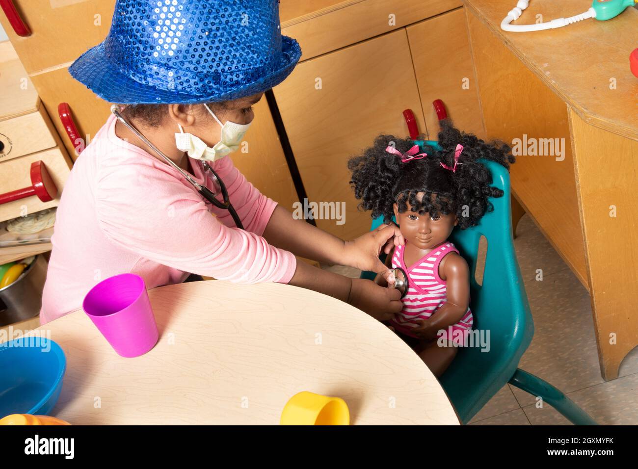 Istruzione Preschool 3-4 anni fingono di giocare in famiglia area, ragazza utilizzando stetoscopio su bambola, indossare cappello e maschera viso vs virus Covid-19 Foto Stock