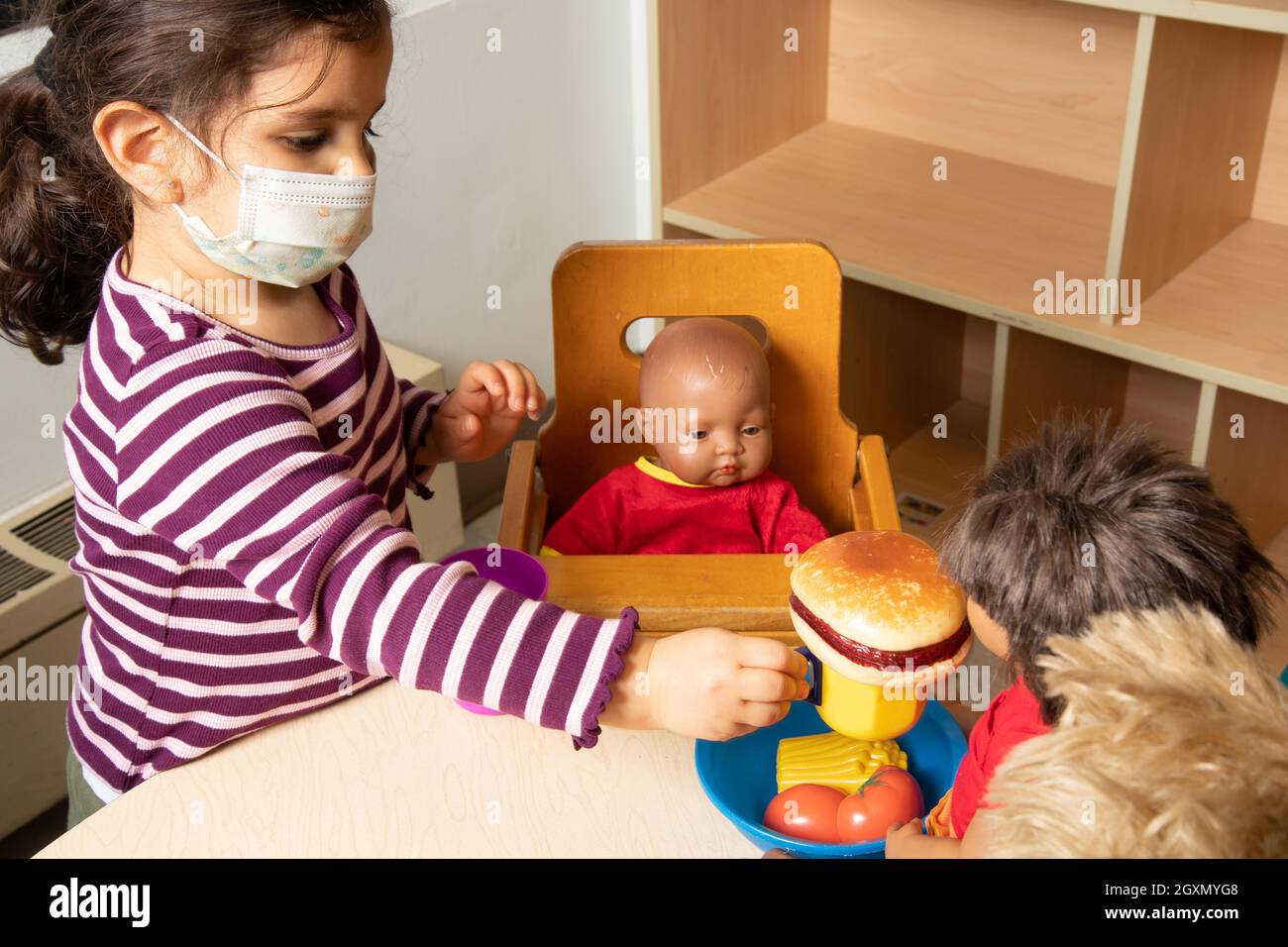 Istruzione Preschool 3-4 anni fingono di giocare in famiglia, bambola che allattano con cibo da gioco, indossare maschera per il viso per proteggere contro Covid-19i Foto Stock