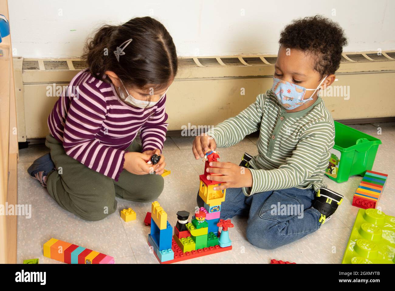 Istruzione Preschool 3-4 anni ragazzo e ragazza giocare insieme con blocchi di plastica di collegamento (Duplo), indossare maschere per il viso per proteggere contro Covid-19 Foto Stock