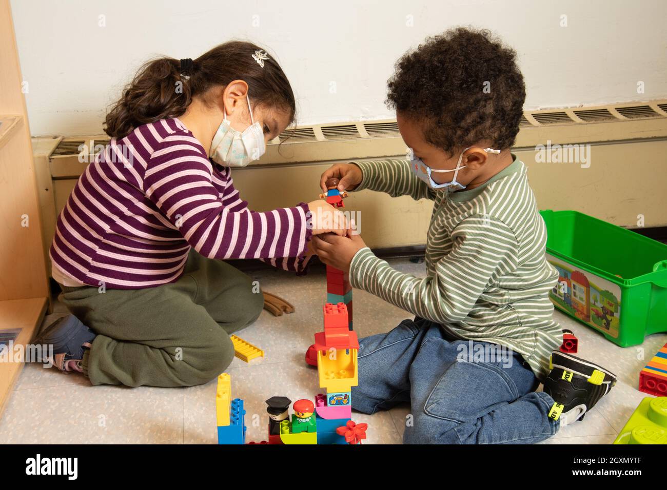 Istruzione Preschool 3-4 anni ragazzo e ragazza giocare insieme con blocchi di plastica di collegamento (Duplo), indossare maschere per il viso per proteggere contro Covid-19 Foto Stock