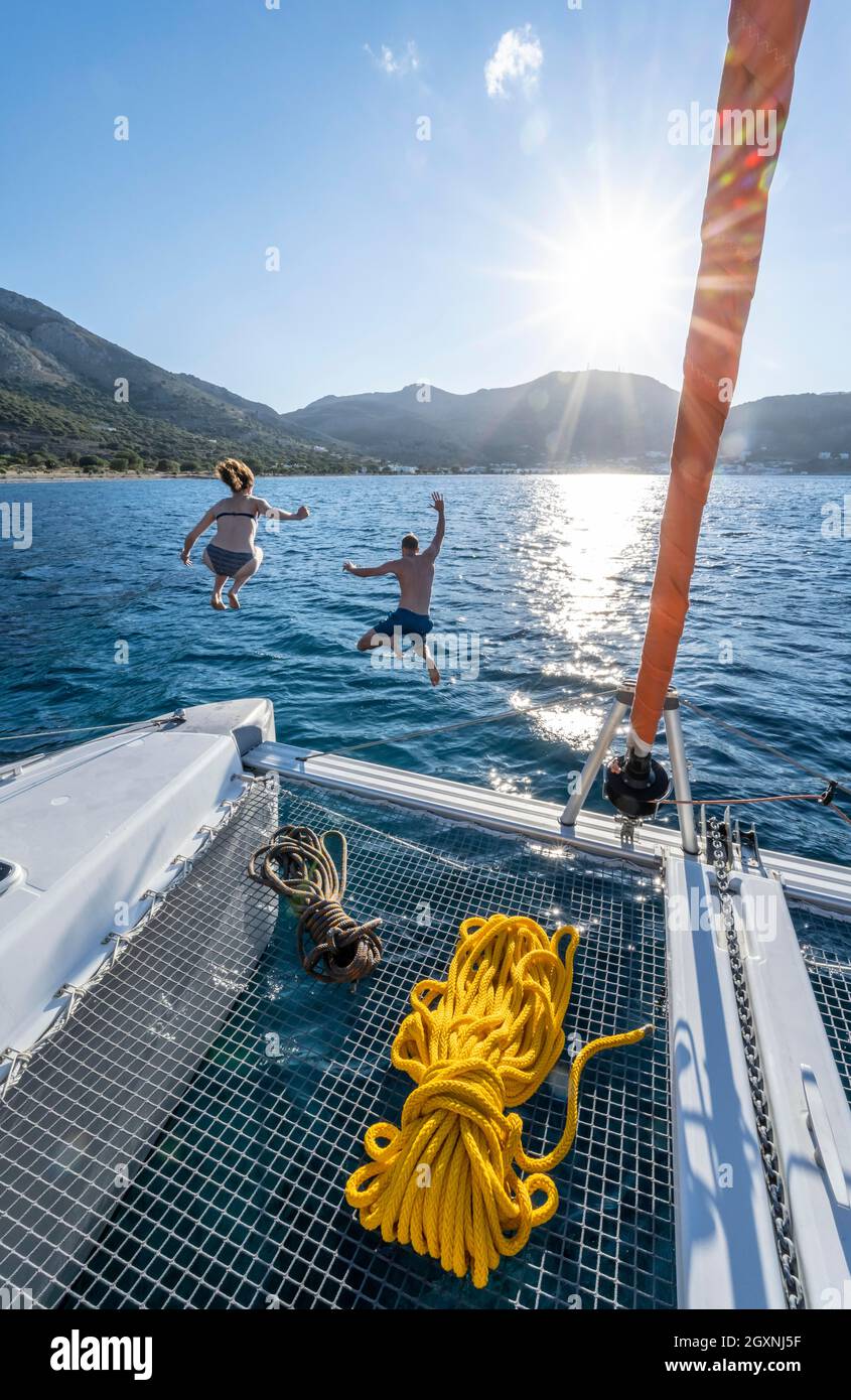 Giovane donna e giovane uomo che salta in acqua, corde su un catamarano a vela, Sun Star, viaggio a vela, Tilos, Dodecaneso, Grecia Foto Stock