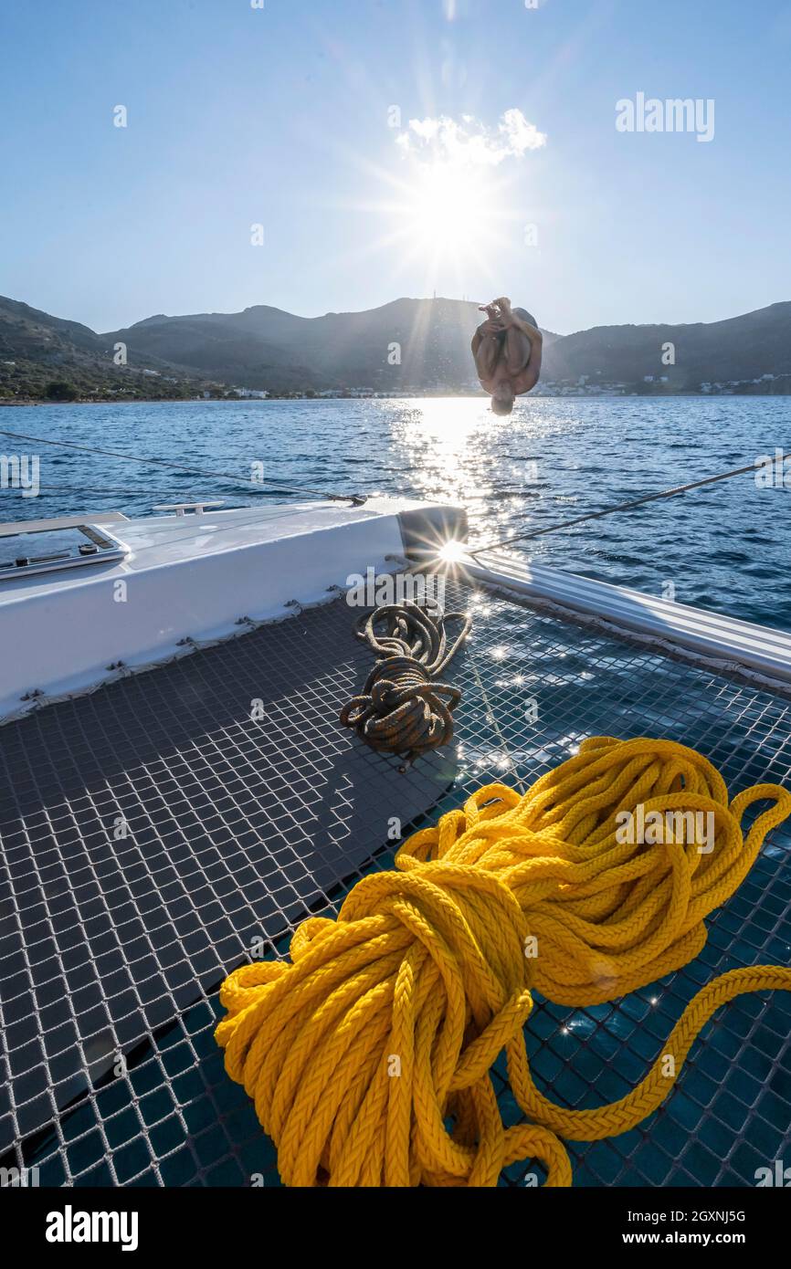 Giovane uomo fa un somersault, salta in acqua, corde su un catamarano a vela, Sun Star, viaggio a vela, Tilos, Dodecaneso, Grecia Foto Stock