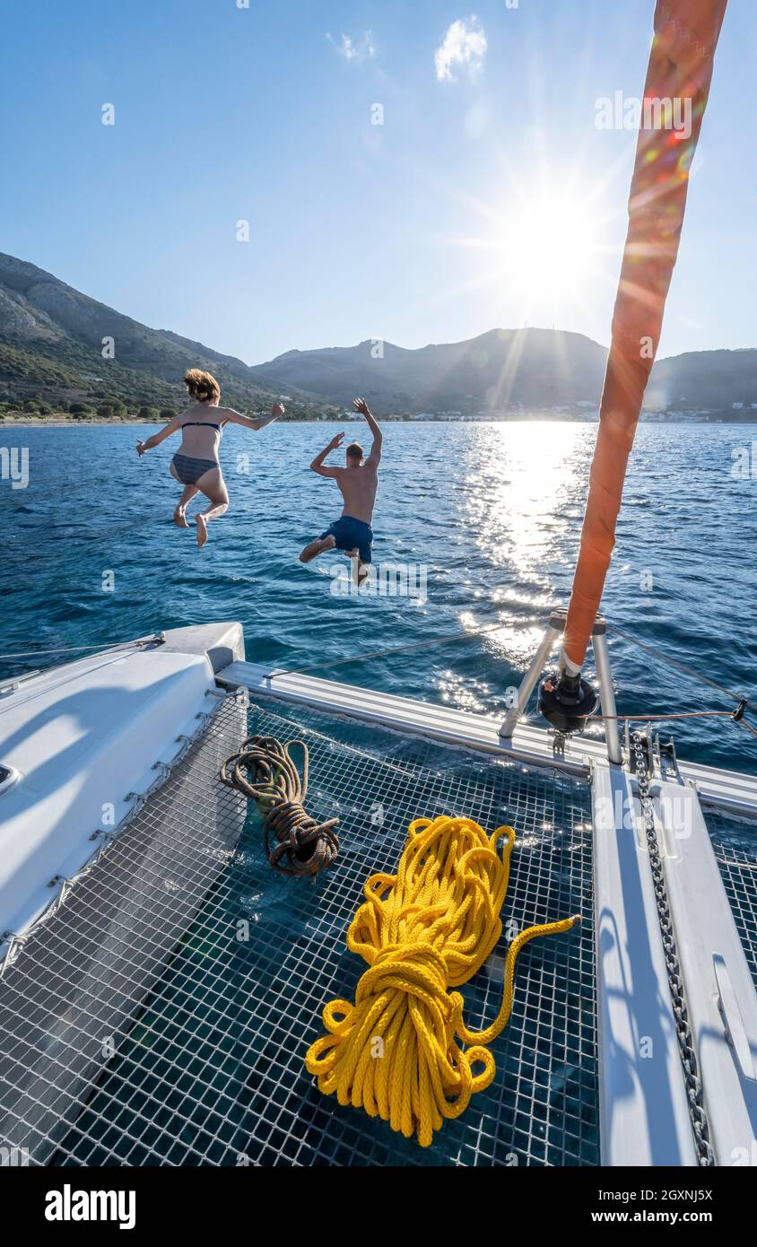 Giovane donna e giovane uomo che salta in acqua, corde su un catamarano a vela, Sun Star, viaggio a vela, Tilos, Dodecaneso, Grecia Foto Stock