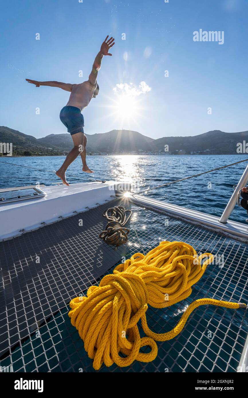 Il giovane uomo salta in acqua, corde su un catamarano a vela, Sun Star, gita in barca a vela, Tilos, Dodecaneso, Grecia Foto Stock