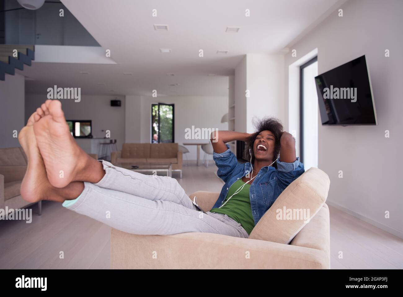 Giovani belle americano africano donna ama ascoltare la musica con le cuffie e tablet in poltrona nella sua casa di lusso Foto Stock