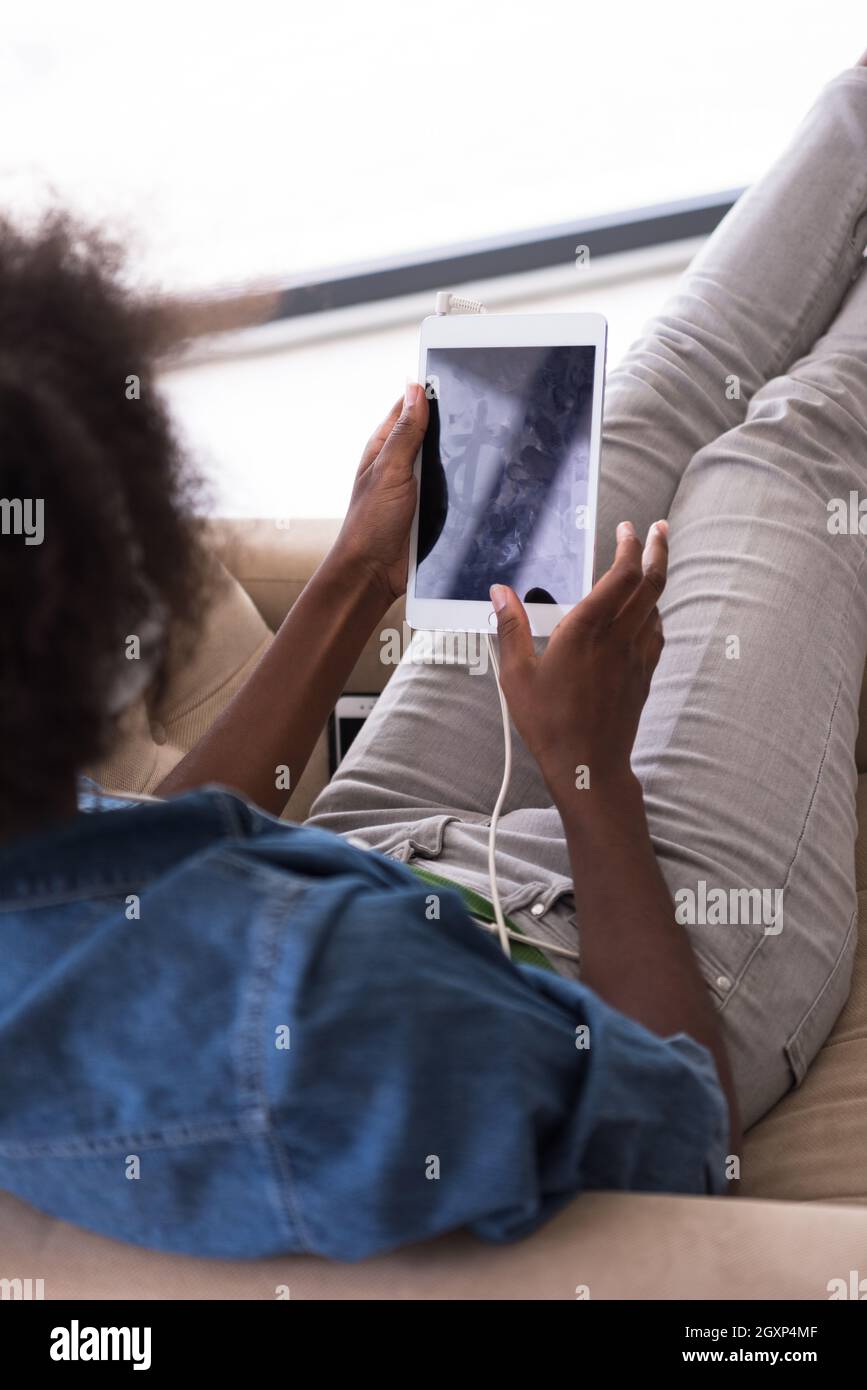 Giovani belle americano africano donna ama ascoltare la musica con le cuffie e tablet in poltrona nella sua casa di lusso Foto Stock