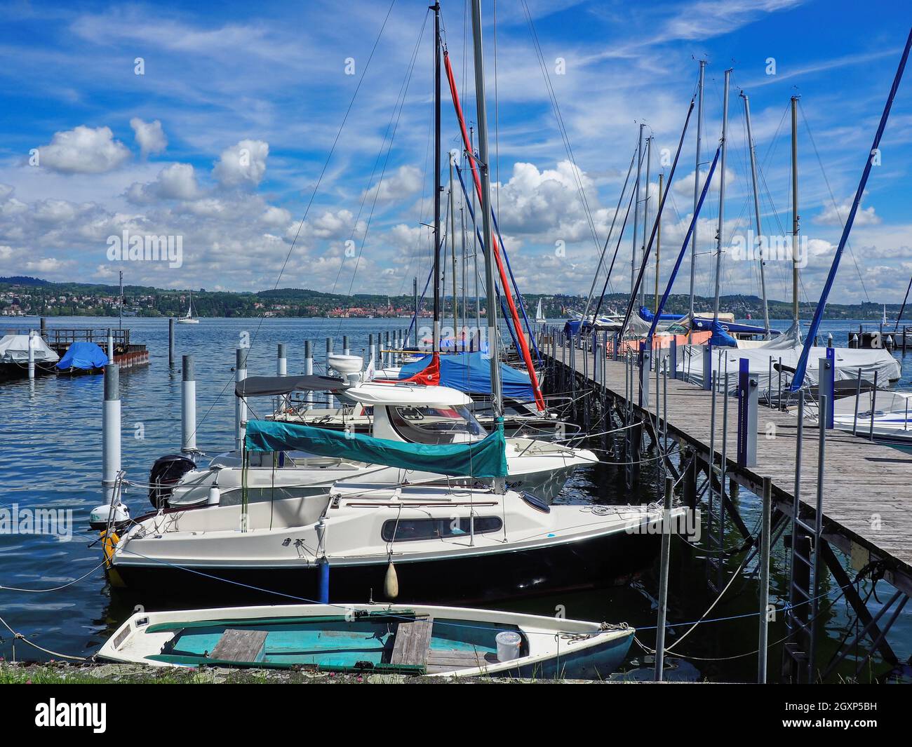 Un molo in legno sul lago di Costanza, in Germania, con piccole barche a vela ormeggiate. Cielo blu estivo con nuvole bianche tufted. Foto Stock