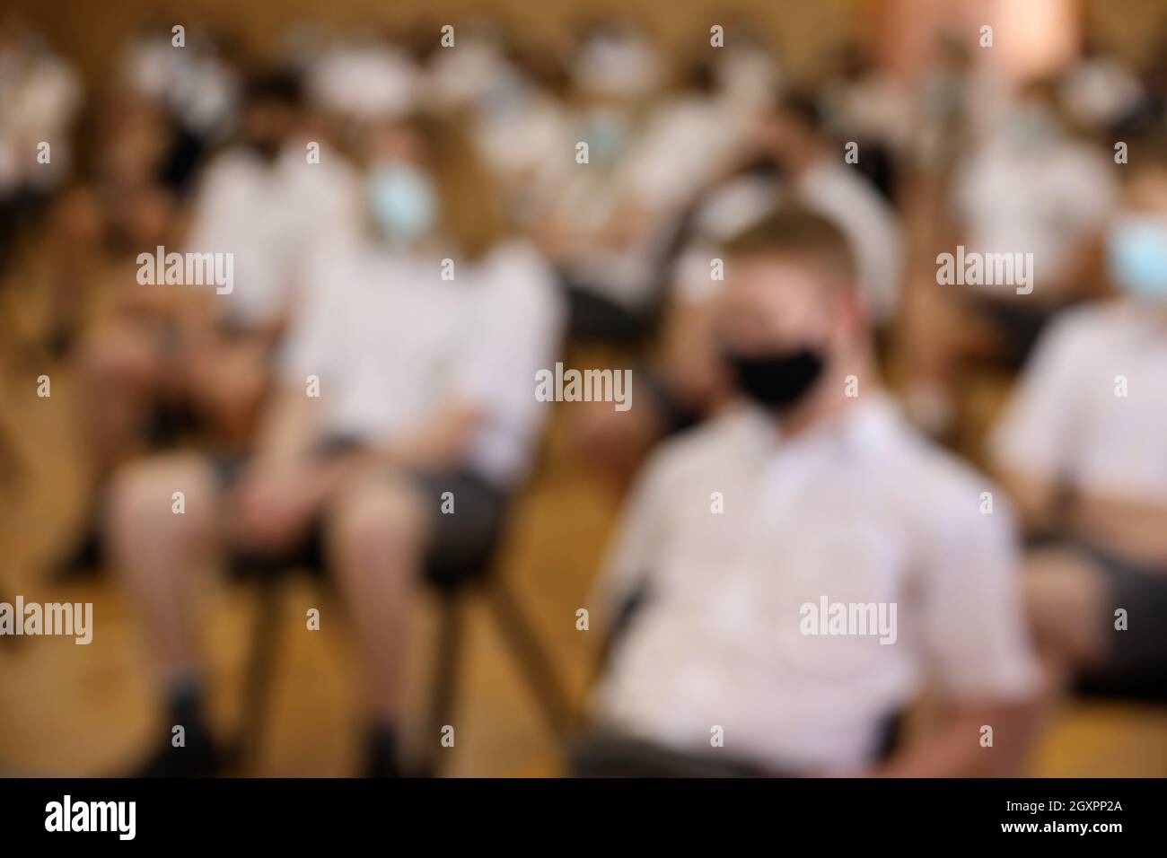 Un'immagine sfocata intenzionale degli studenti delle scuole superiori seduti socialmente a distanza indossando maschere facciali blu e nere. Scuole sicure covid. Conformità Foto Stock
