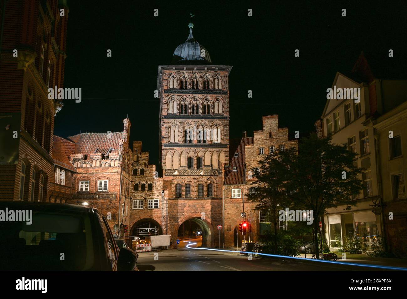 Lubeck Burgtor torre d'ingresso di notte e una leggera traccia di una bicicletta che attraversa, storico edificio in mattoni delle mura della città e le case nel o Foto Stock