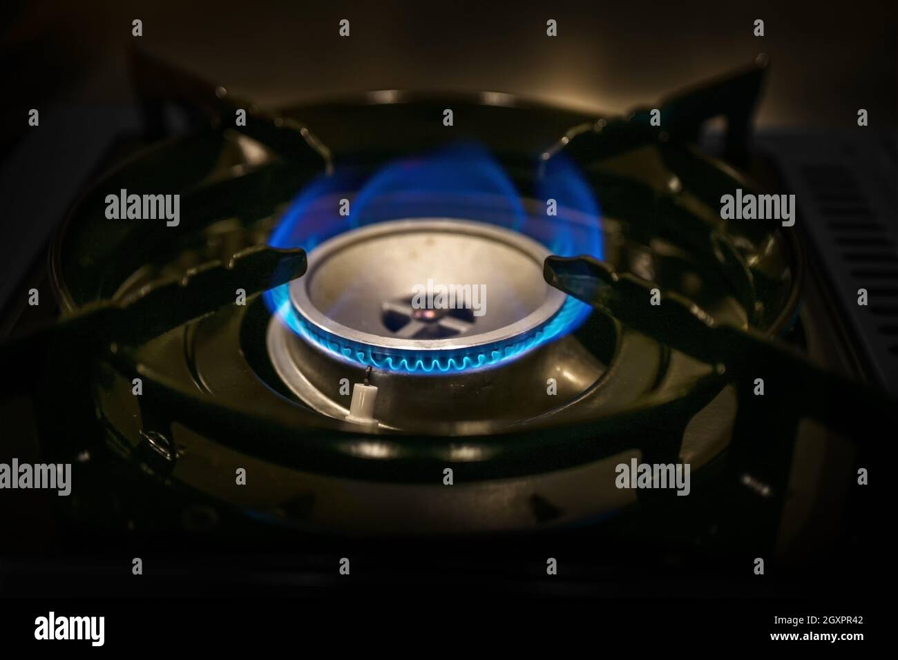 fiamma di gas blu su una stufa da cucina, costi crescenti di combustibile fossile ed energia, tasse di emissione di carbonio per la protezione dell'ambiente e del clima, primo piano scuro Foto Stock