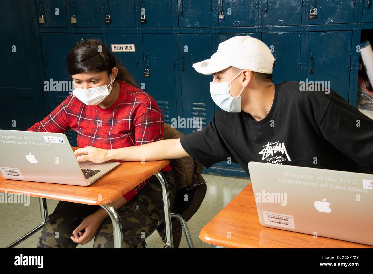 Istruzione High School scena classe maschio studente appoggiarsi sopra per spiegare qualcosa al suo neigbor, entrambi indossare maschere per proteggere contro Covid Foto Stock