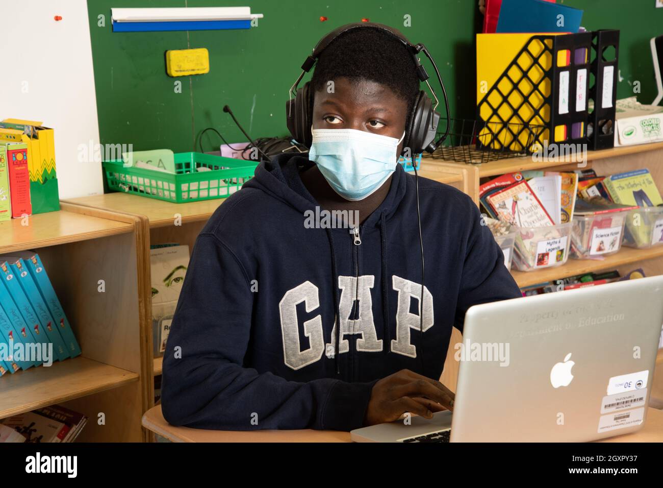 Istruzione studente maschile della High School ascoltare in classe, computer portatile di fronte a lui, indossare maschera per la protezione contro l'infezione Covid-19 Foto Stock