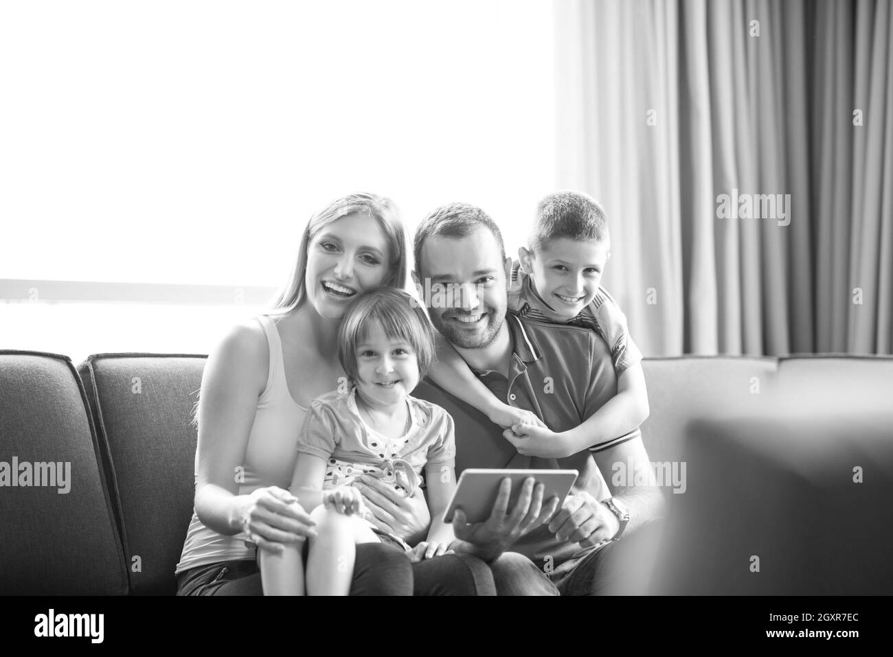 Felice famiglia giovane giocare insieme con la compressa a casa seduti sul divano Foto Stock