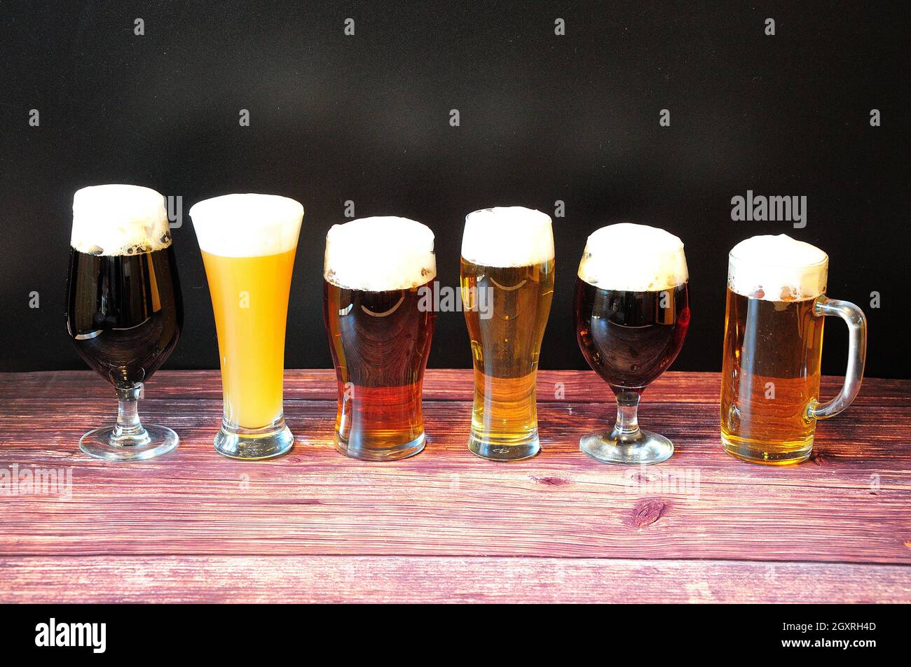 Sei diversi bicchieri di birra con sei diversi tipi di birra con stativo di schiuma in fila su un tavolo di legno. Primo piano. Foto Stock