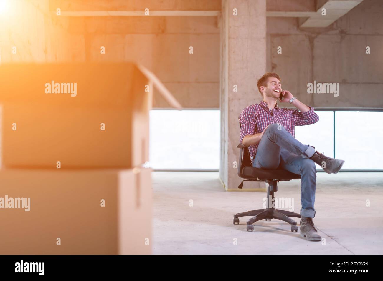 giovane uomo d'affari casual utilizzando un telefono cellulare mentre si fa una pausa in cantiere con la luce del sole attraverso le finestre durante il movimento in una nuova stella Foto Stock