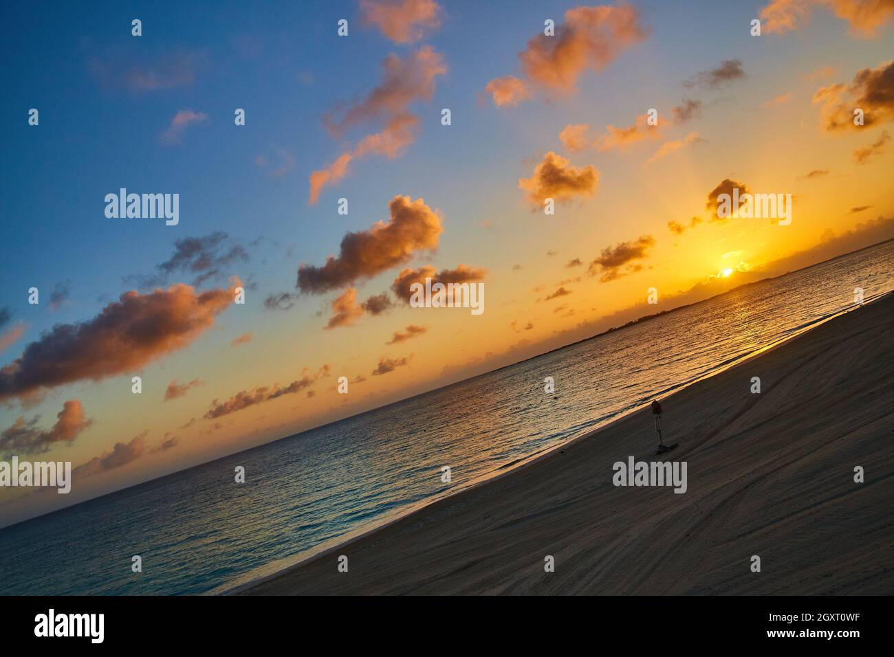 Vista inclinata sulla spiaggia dell'oceano con tramonto o alba e cielo dorato con nuvole rosa Foto Stock