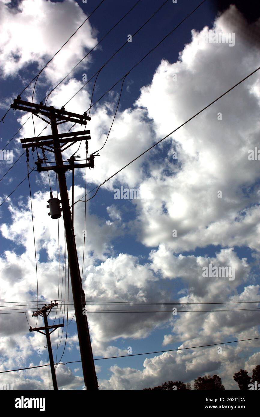 Pali e linee telefoniche contro un cielo blu nuvoloso Foto Stock