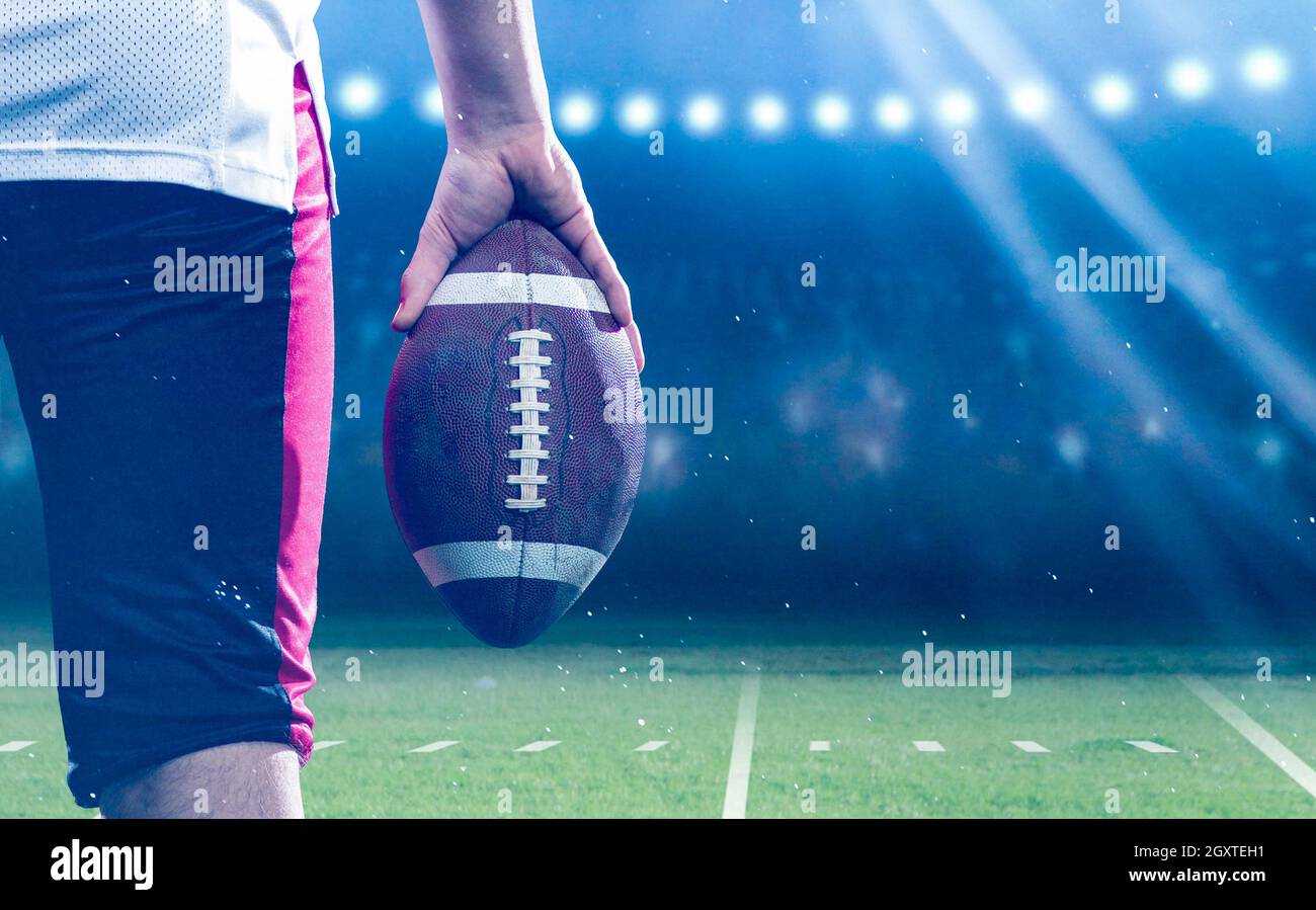 Primo piano vista posteriore del giovane fiducioso giocatore di football americano sul campo moderno con luci e razzi di notte Foto Stock