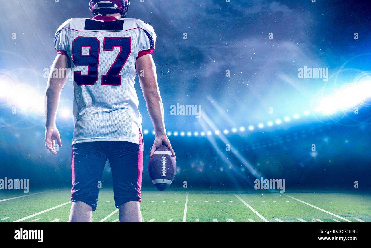Vista posteriore del giovane fiducioso giocatore di football americano sul campo di grande stadio moderno con luci e razzi di notte Foto Stock