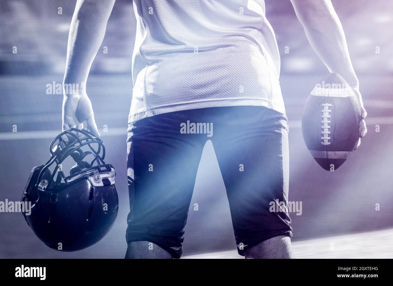 Vista posteriore del giovane fiducioso giocatore di football americano sul campo di notte Foto Stock