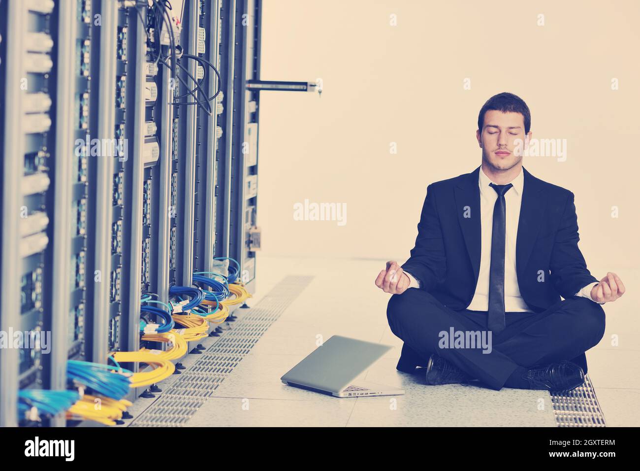 Bel giovane uomo d affari in abito nero e cravatta pratica yoga e relax al server di rete sala mentre in rappresentanza di stres concetto di controllo Foto Stock