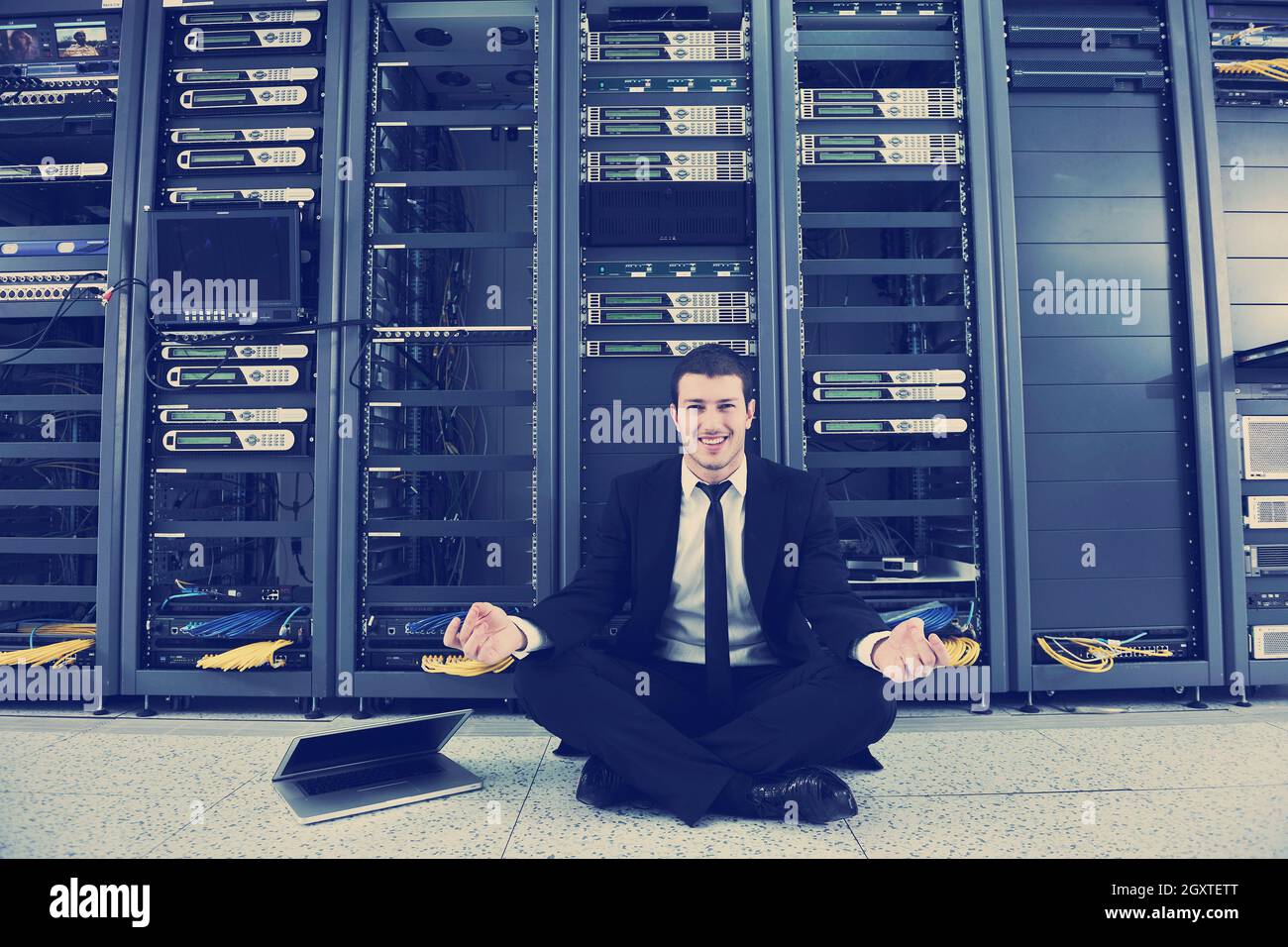 Bel giovane uomo d affari in abito nero e cravatta pratica yoga e relax al server di rete sala mentre in rappresentanza di stres concetto di controllo Foto Stock