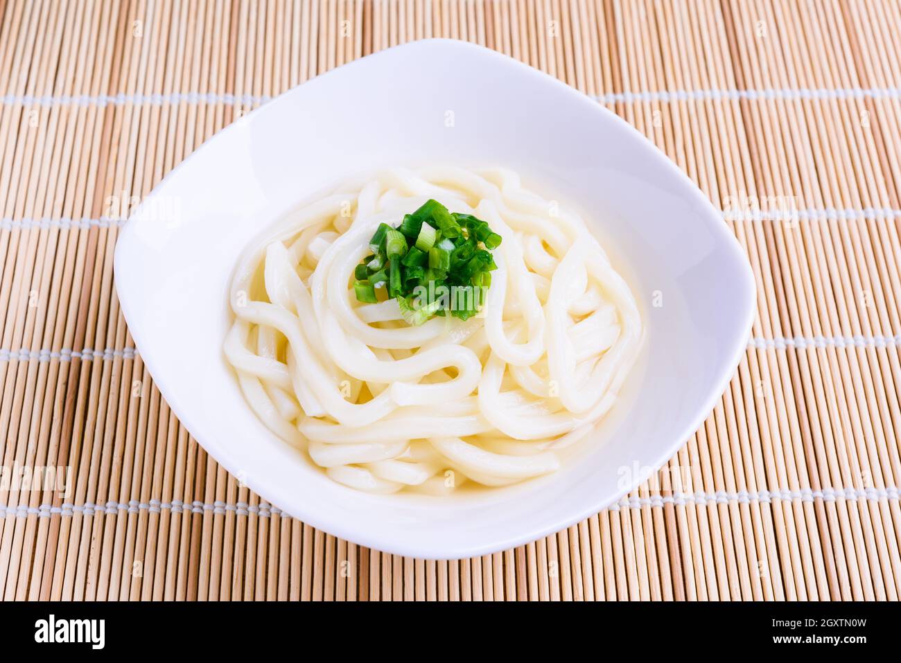 Tagliatelle di udon giapponesi preparate di fresco in ciotola bianca con cipolline guarnite su stuoia di bambù. Foto Stock