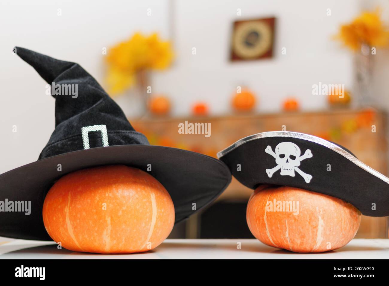 Zucche di Halloween con streghe e cappelli pirata sul tavolo sullo sfondo di un camino rustico casa con decorazioni autunnali. Foto Stock