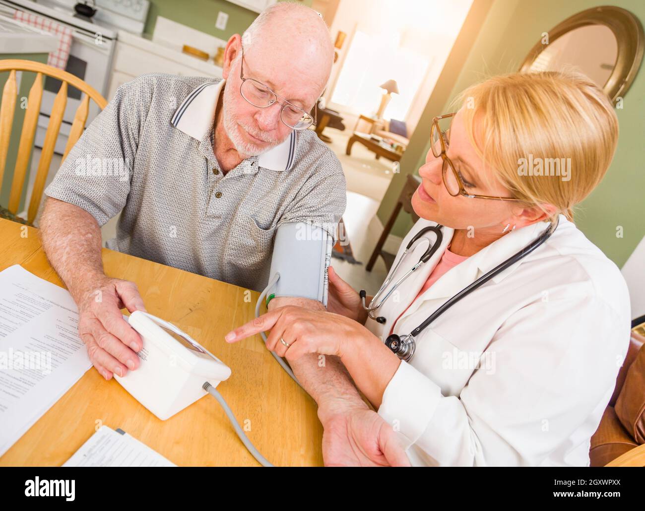 Femmina di infermiere o medico aiutando Senior Adulto Uomo prende la pressione sanguigna in casa. Foto Stock