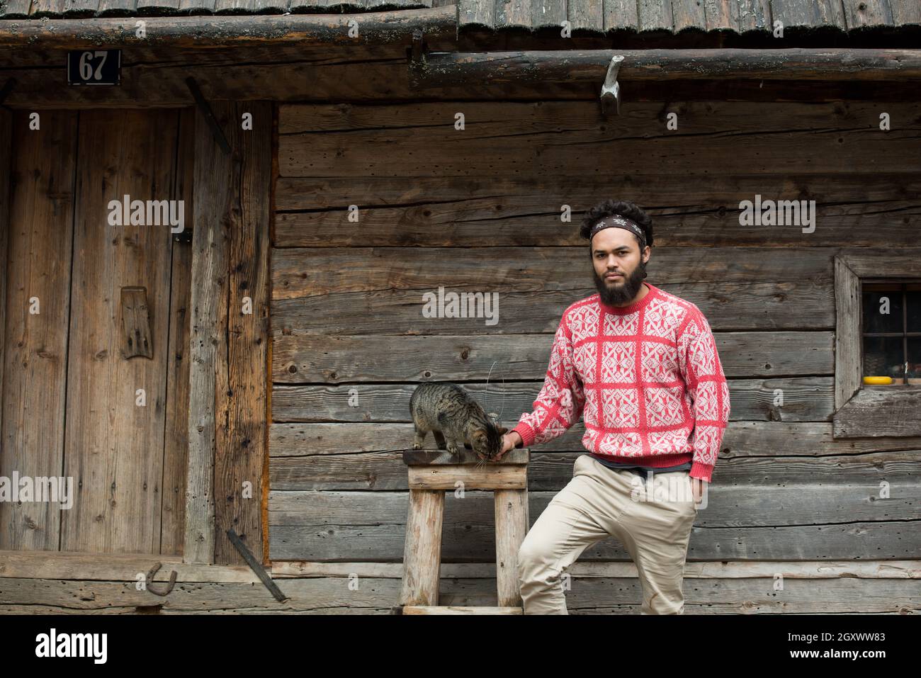 Ritratto di giovane hipster l uomo con la barba e il gatto nella parte anteriore della casa in legno Foto Stock