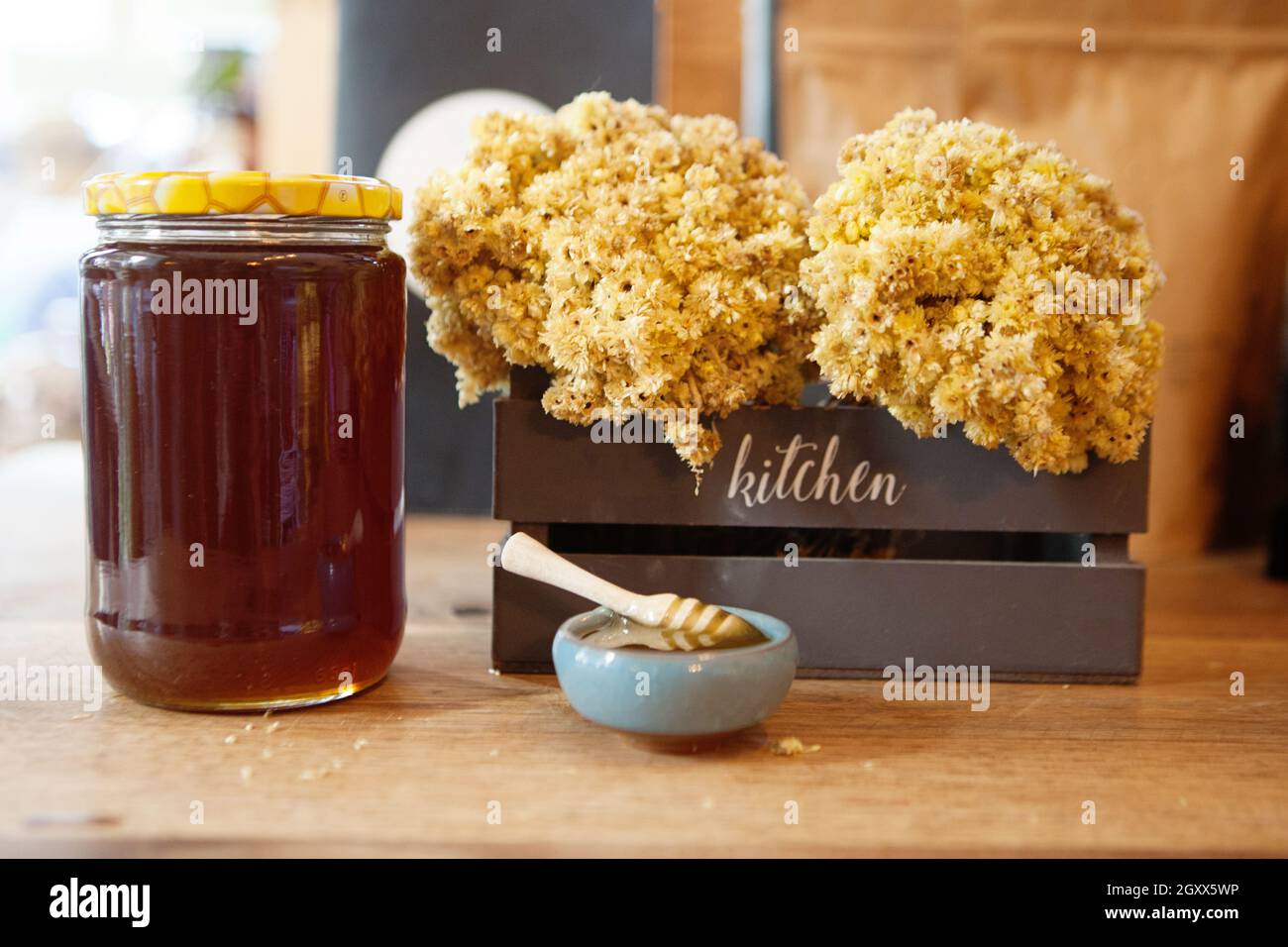 Cucchiaia di miele in una ciotola di miele vicino ad un vaso di miele e fiori di mimosa in una cassa Foto Stock