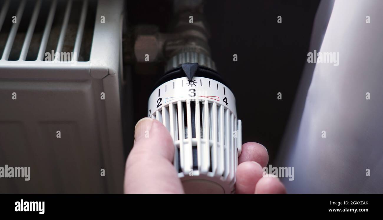 abbassare il termostato sul radiatore per risparmiare energia grazie all'aumento dei costi di riscaldamento Foto Stock