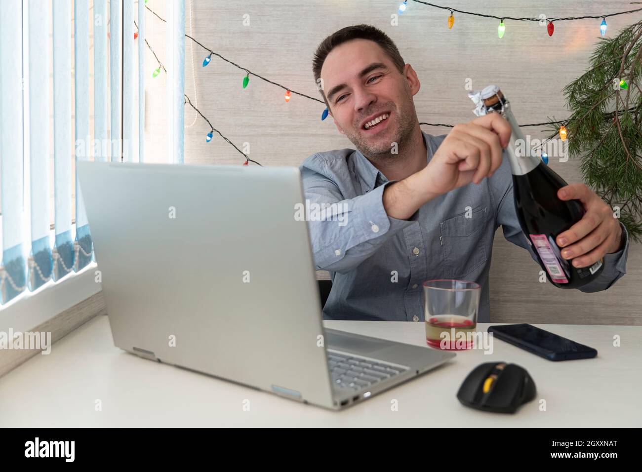 L'impiegato dell'ufficio festeggia il Natale al lavoro. Festeggiamo Natale e Capodanno sul posto di lavoro. Un lavoratore di ufficio beve alcol. Comunicazione remota. Foto Stock