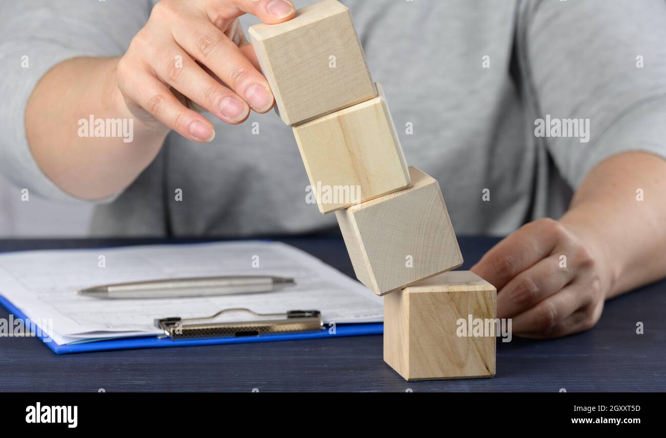 la mano femmina tiene i cubetti cadenti sul tavolo. Il concetto di crisi di un manager, mantenendo a galla l'azienda, stabilizzando l'impresa. Sviluppo s Foto Stock